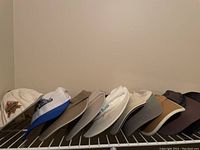 Selection of hats and ball caps including white and beige styles, some with logos and brand names, arranged on a rack.