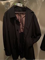 Front view of the black Baumler coat hanging, showing buttons and outer pockets.
