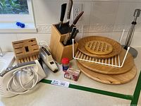 Photo showing two wooden knife blocks with knives, electric cutting tool, two lazy susans, metal paper towel holder, and other small kitchen items on a counter surface near a window.