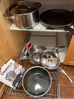 Full view of multiple pots and pans including a large pot with lid, a frying pan and kitchen accessories such as a grater and SimmerMat box
