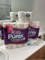 Photo of Purex Ultra 60-roll 3-ply toilet paper pack with Royale Velour pack and box of disposable face masks on bathroom counter.