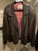 Front view of vintage brown leather jacket on hanger, shows open zippered front and pinkish lining.
