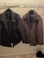 Two men's winter coats hanging side by side, the left one is a black Claiborne quilted jacket, the right one is a brown Dockers suede look jacket with fleece collar.