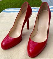 Pair of red Christian Louboutin Fifi 100 pumps with glossy patent finish, 4 inch stiletto heels. Showing wear on soles and fading interior logo.