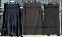 Three skirts hanging on a fence: navy blue pleated knit skirt, black pencil skirt, black pleated knit skirt