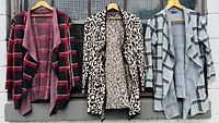Three vintage Jones New York front drape cardigans hanging side by side: red/black plaid, leopard print, and gray/black plaid patterns.