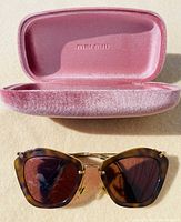 Pink crushed velvet Miu Miu sunglass case with embossed logo inside, paired with tortoiseshell cat eye sunglasses with brown lenses and gold accents.