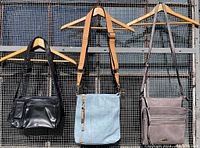 Three handbags hanging on wooden hangers against a metal mesh background showing front views of all three bags.