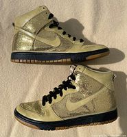 Pair of beige and metallic gold sequinned Nike SB Dunk High women's sneakers from 2009 showing side profile.
