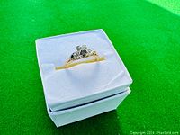 Ring displayed in white box on green surface
