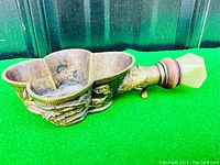 Side view of the brass silk iron showing detailed dragon relief and faceted jade handle on green background.