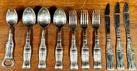 Full view of the entire set of flatware pieces including 3 knives, 4 forks, 3 spoons, and 1 spork with bottle opener handle, all with Coca-Cola bottle shaped handles.
