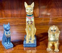 Three Egyptian-themed statues: dark Bastet cat, larger gold Bastet cat with painted details, and small gold sphinx.