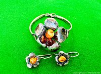 Bracelet and earrings on a green background, showing detailed front view of bracelet's flower with amber stones and one earring