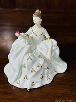Front view of the Royal Doulton figurine showing the seated woman in white dress with gold details and holding a pink flower.