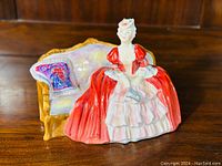 Front view of Royal Doulton figurine showing woman in red and white dress sitting on a couch with colorful cushion.