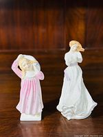 Two Royal Doulton figurines displayed side by side on wooden surface, showing overall appearance and size comparison