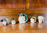 Full set of 5 Royal Doulton Toby jugs arranged on wooden surface showing front details of each jug