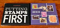 Two closed Royal Mail stamp books side by side: 'PUTTING STAMPS FIRST' with black cover and 'ALONG THESE LINES' with purple cover showing stamp images.
