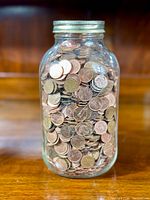 Front view of a glass sealer jar filled to the top with old Canadian pennies sitting on a wooden surface.