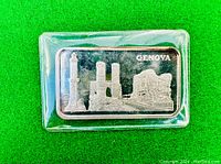 Front side of silver bar showing city of Genoa design and 'GENOVA' inscription, sealed in plastic case.