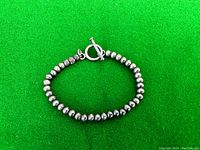 Sterling silver ball bead bracelet laid flat on green background showing toggle clasp and round beads.