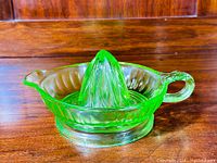 Front view of a bright green uranium glass juicer with a reamer cone and round handle on the right side, placed on a wooden surface.