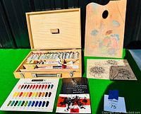 Full view of wooden artist box open with Reeves oil paint tubes, wooden palette, plants prints, color chart and instruction booklet laid beside it