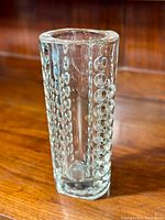 Front side view of clear pressed glass vase showing bubble pattern on vertical sides, thick base, and circular opening.