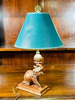 Full view of the vintage mahogany elephant table lamp with green lampshade and brass finial on wooden surface against wooden background.