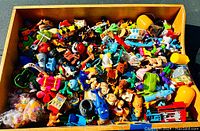 Overview of a large wooden tray filled with vintage small plastic Kinder toys including figures, vehicles and accessories.