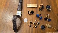 Top-down view of watch, money clip, cufflinks, studs and tie pin arranged on table