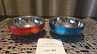 Two snack bowls side by side on a decorative metal mat, one red and one blue with shiny stainless steel inner lining.