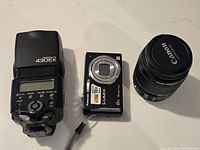 Canon Speedlite 430EX flash, Panasonic Lumix camera, and Canon 18-55mm lens on white surface showing front and top sides.