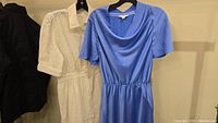 Both dresses hung on hangers: white BA&SH eyelet dress with button-front and collar, and blue Vince dress with cowl neckline.