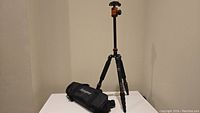 Full view of assembled tripod with carrying bag placed beside it on a white surface.