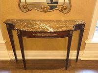 Front view of the marble top console table against a wall, showing the marble shape and brass detailing on the base.