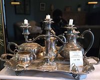 Full front view of tea set and three-arm candelabra arranged on ornate silver-plated tray showing all items clustered together.
