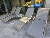 Four slingback chaise lounge chairs arranged on a stone patio near a glass wall