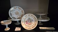 Six porcelain dishes featuring hand painted floral center designs with pink and purple flowers. Gold filigree border patterns and gold trim edges. Includes three pedestal candy dishes and three flat plates, varying sizes with maximum diameter around 10 inches. All made in France.
