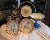 Wide shot showing a variety of porcelain candy dishes, pedestals, plates with floral and gold accents.