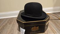 Vintage black Stetson bowler hat displayed on original hexagonal Stetson box with gold crest and trim, showing lot label