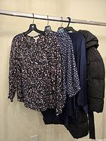 Side view showing black puffer jacket and three printed tops on hangers