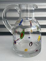 Front left angle view of clear glass pitcher with colorful spots