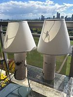 Front view of both lamps on glass table with city skyline background