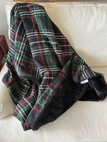 Image showing the full plaid blanket draped on a beige sofa, highlighting the plaid pattern and black faux fur lining edge.