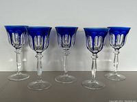 Five cobalt blue cut-to-clear crystal wine goblets in a row against white background