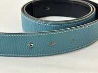 Close-up of turquoise pebbled leather side with visible holes and white stitching.