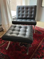 Front view of black vinyl Barcelona chair paired with matching ottoman on red patterned rug near window