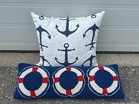 Square pillow with blue anchors on white background and rectangular pillow with blue background and life buoy rings shown against grey garage door.